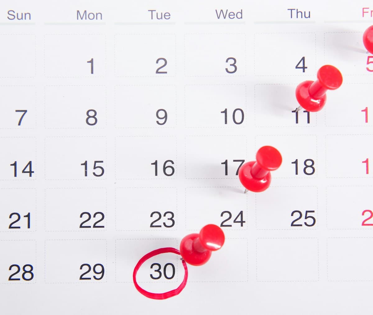 Wall calendar with red push pins marking working days and deadlines