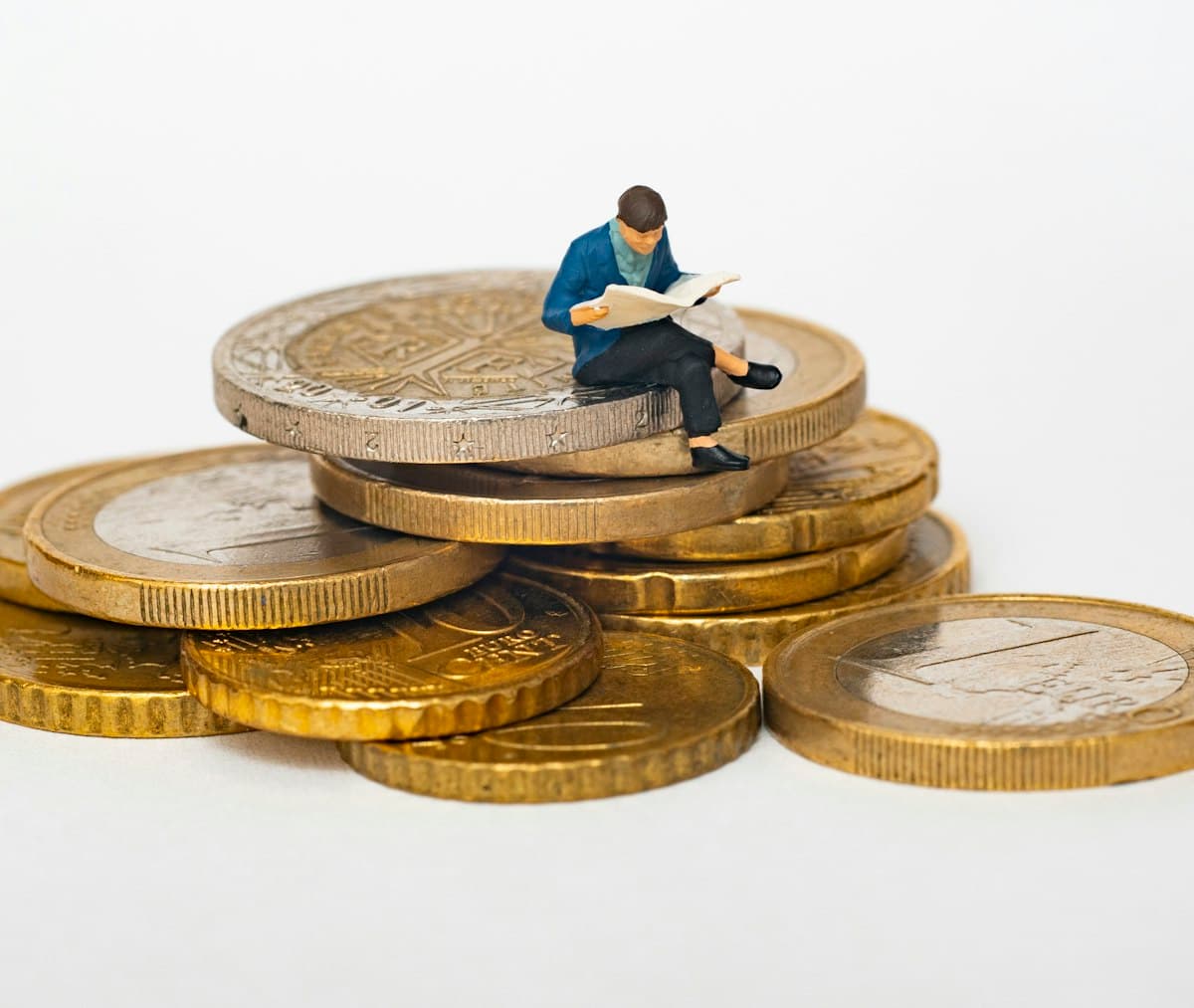 Miniature figure sitting on a stack of coins reading a newspaper