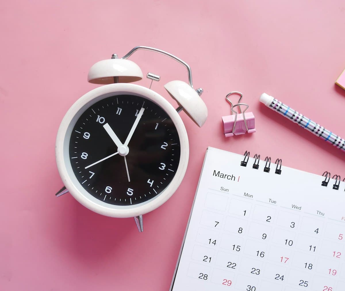White and pink analog alarm clock on a table as time passes between dates