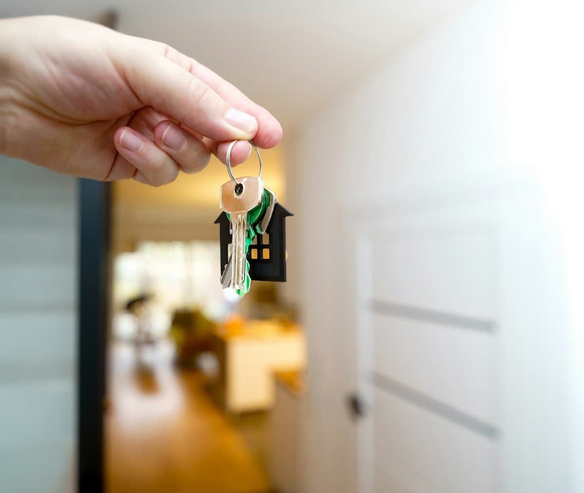 Hand holding house keys in front of the entrance of a new home