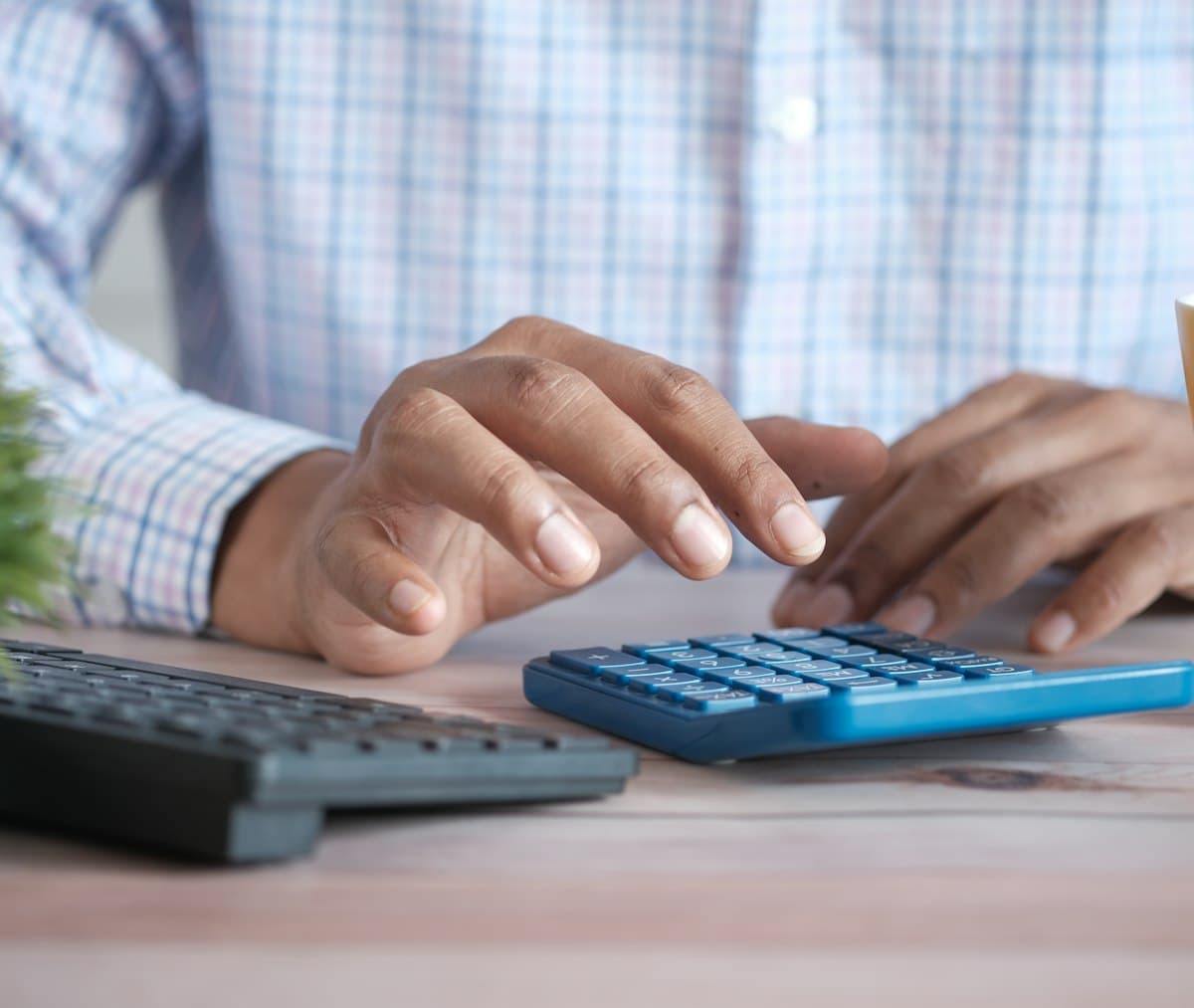 Person using a calculator at a desk beside a coffee mug to work out margins
