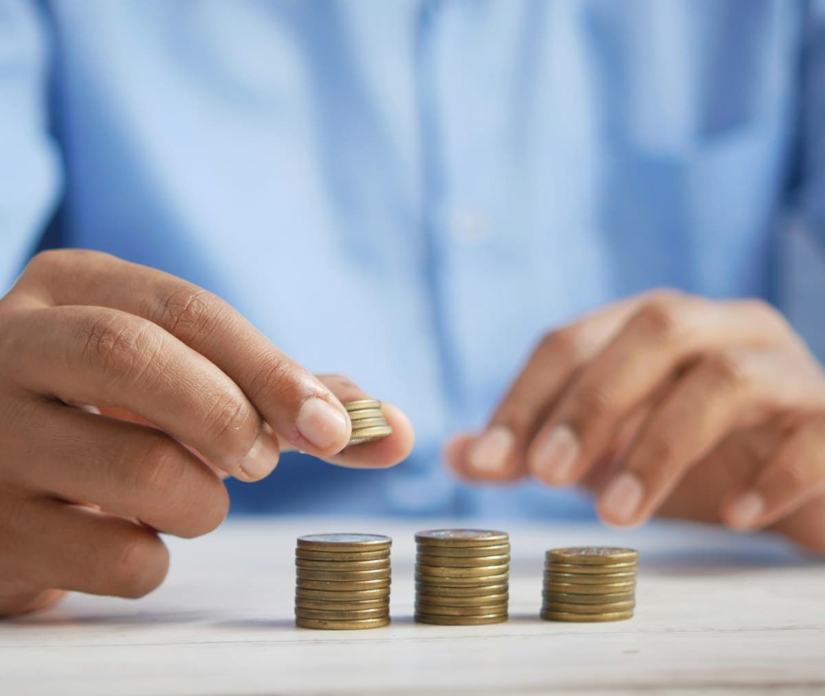 Person stacking coins on a table to build up savings over time