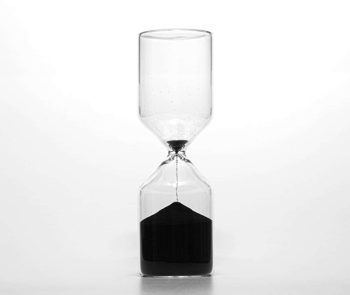 Clear glass hourglass with dark sand measuring the passing of hours