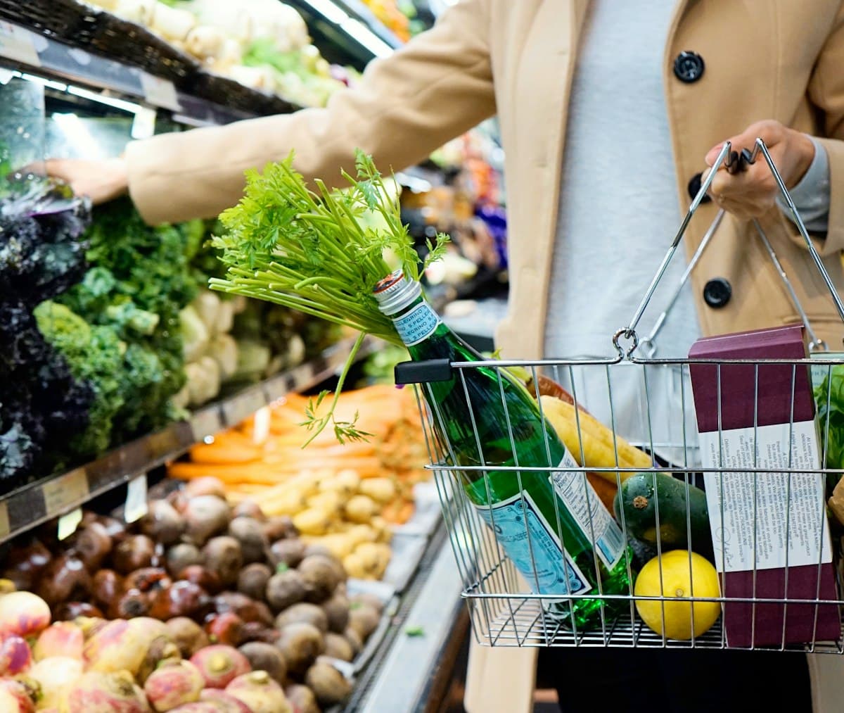 Shopper holding a green shopping cart while comparing prices in a grocery store