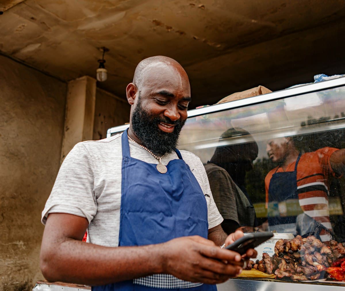 Small business owner in an apron looking at a phone to check sales